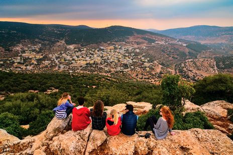 Eine Gruppe junger Menschen sitzen auf einem Felsen und schauen über die Stadt Ajloun und das grüne Jordantal in Jordanien