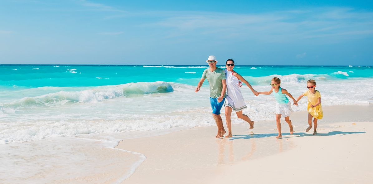 Eine Familie mit zwei Kindern läuft fröhlich durch die Wellen am Strand
