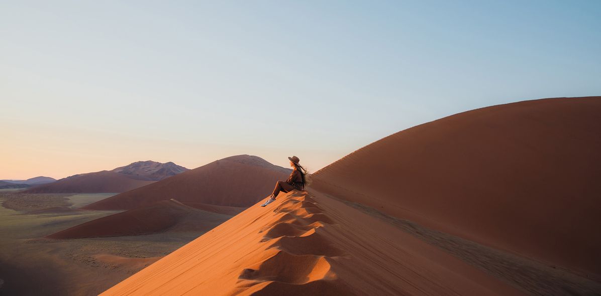 Frau sitzt in der Wüste im Namib Naukluft Nationalpark in Namibia und genießt den Ausblick