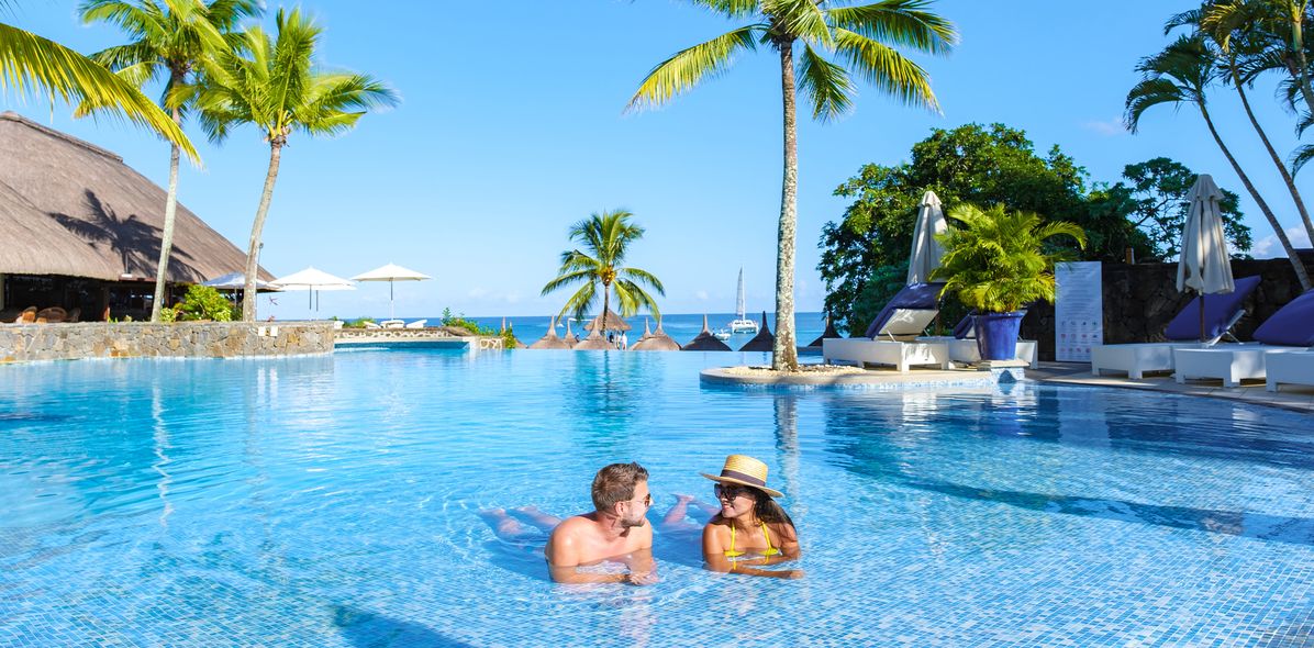 Paar entspannt im Pool eines Hotels auf Mauritius mit Palmen und Meerblick