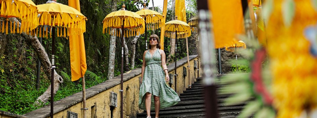 Frau geht eine Tempeltreppe im GWK Cultural Park auf Bali zwischen traditionellen gelben Schirmen hinunter