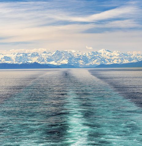 Blick auf die Fahrspur eines Kreuzfahrtschiffs im Prince William Sound mit schneebedeckter Bergkulisse in Alaska