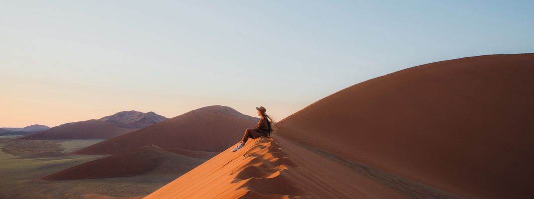 Frau sitzt in der Wüste im Namib Naukluft Nationalpark in Namibia und genießt den Ausblick