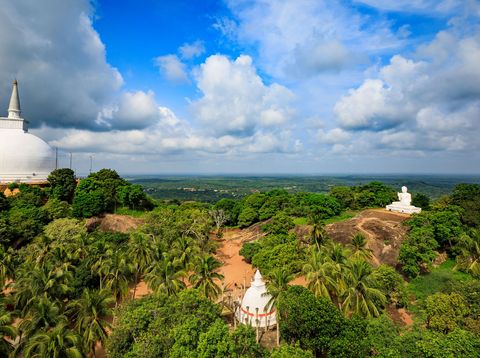 Weiße Stupa von Mihintale in Sri Lanka, umgeben von üppigem Grün und Felsen unter einem weiten Himmel mit Wolken