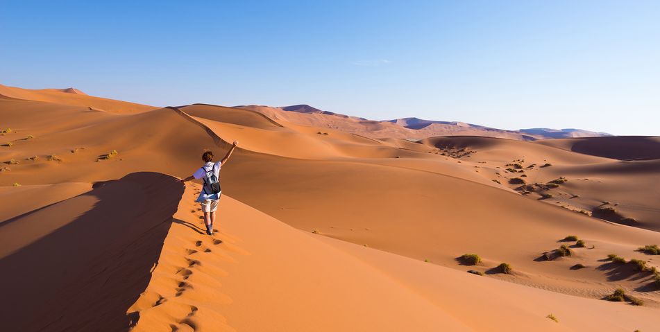 Frau mit Rucksack geht durch die typisch rotgefärbte namibische Wüste im Namib-Naukluft-Nationalpark