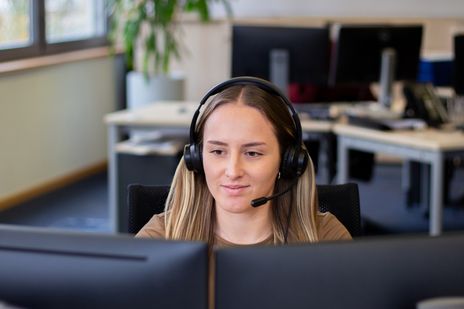 Auszubildende Olivia sitzt an ihrem Arbeitsplatz und telefoniert mit Kunden