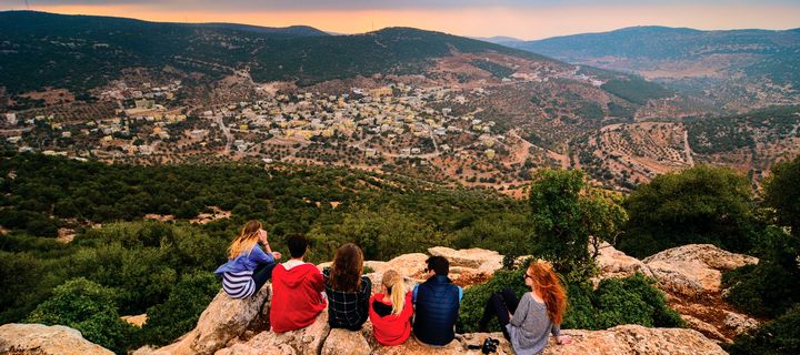 Eine Gruppe junger Menschen sitzen auf einem Felsen und schauen über die Stadt Ajloun und das grüne Jordantal in Jordanien