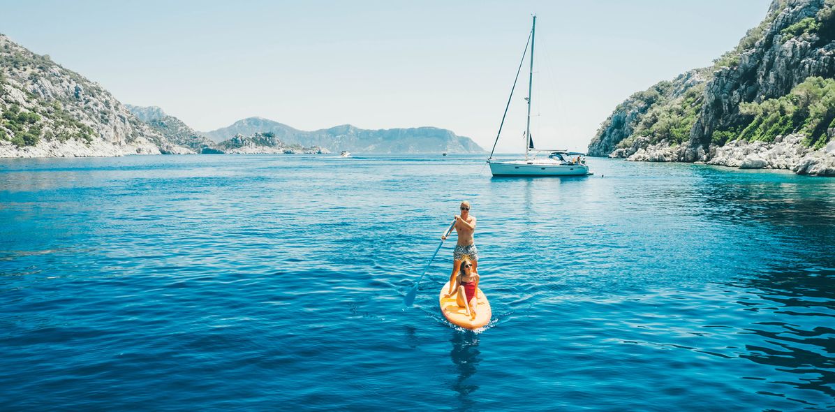 Paar auf einem Stand-up-Paddle in einer türkisblauen Bucht