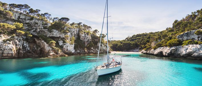 Boot in der Bucht Cala Macarella auf Menorca mit klarem, türkisblauem Wasser, umgeben von Felsen und Pinien