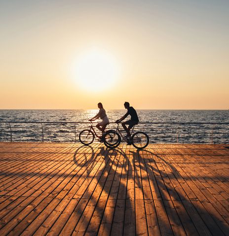 Paar beim Radfahrten an der Promenade im Sonnenuntergang