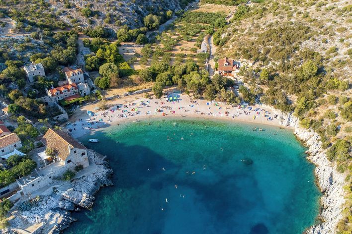 Luftaufnahme der Bucht Dubovica auf der Insel Hvar in Kroatien mit Kiesstrand, Steinhäusern und klarem Wasser