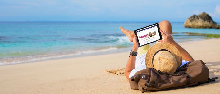 Mann liegt am Meer im Sand und liest auf dem Tablet