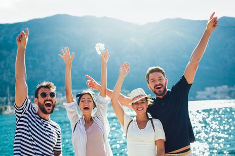Gruppe junger Menschen springt lachend am Meer bei Sonnenschein