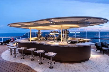 Moderne Skybar an Bord der MSC Seascape mit rundem Bartresen, Sitzgelegenheiten und Meerblick bei Abenddämmerung