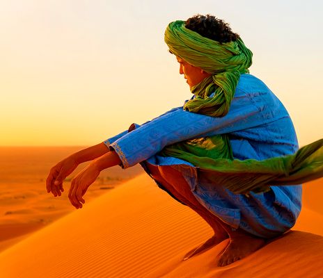 Blick auf einen traditionell gekleideten Mann sitzend in den roten Dünen der Sahara 