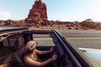 Frau im Cabrio vor roter Felslandschaft im Arches Nationalpark in den USA