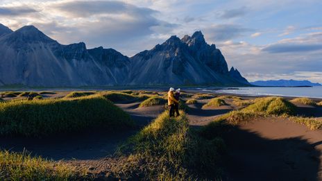 Paar in der Landschaft von Stokksnes auf Island bei Sonnenschein mit Dünen, Strand und Bergkulisse