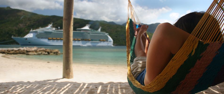 Frau liegt in einer Hängematte am Meer mit Blick auf ein Kreuzfahrtschiff im Sommer
