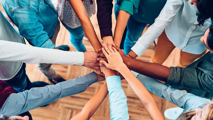 Mehrere Hände treffen sich zur Stapelgeste, Team zeigt Zusammenhalt in der Mitte