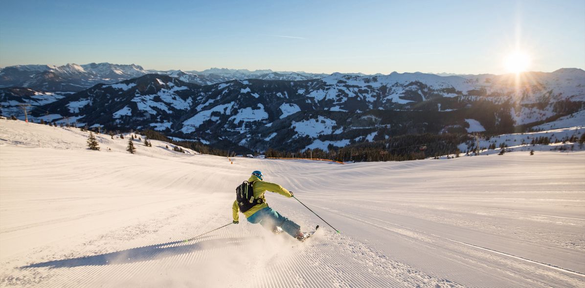 Skifahrer von hinten bei rasanter Abfahrt auf sonnenbestrahlter Piste