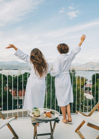 Zwei Frauen genießen den Ausblick von ihrem Hotel-Balkon auf einen Hafen