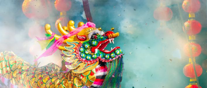 Bunter chinesischer Drachenkopf bei einer Festparade mit roten Laternen im Hintergrund