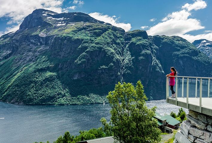 Eine Frau steht auf einer Aussichtsplattform und schaut auf den Geirangerfjord