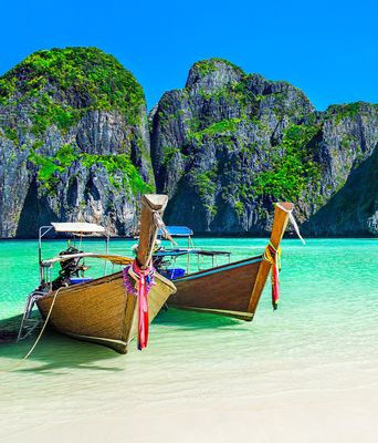 Longtailboot liegt im türkisfarbenen Wasser vor Kalksteinfelsen auf Koh Phi Phi