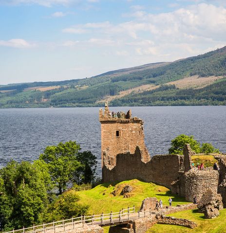 Urquhart Castle am Ufer von Loch Ness mit Blick über den See und die umliegenden Highlands