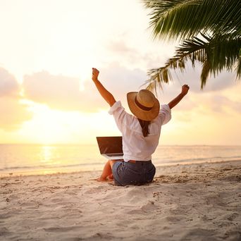 Frau sitzt im Sand und hat einen Laptop auf dem Schoß