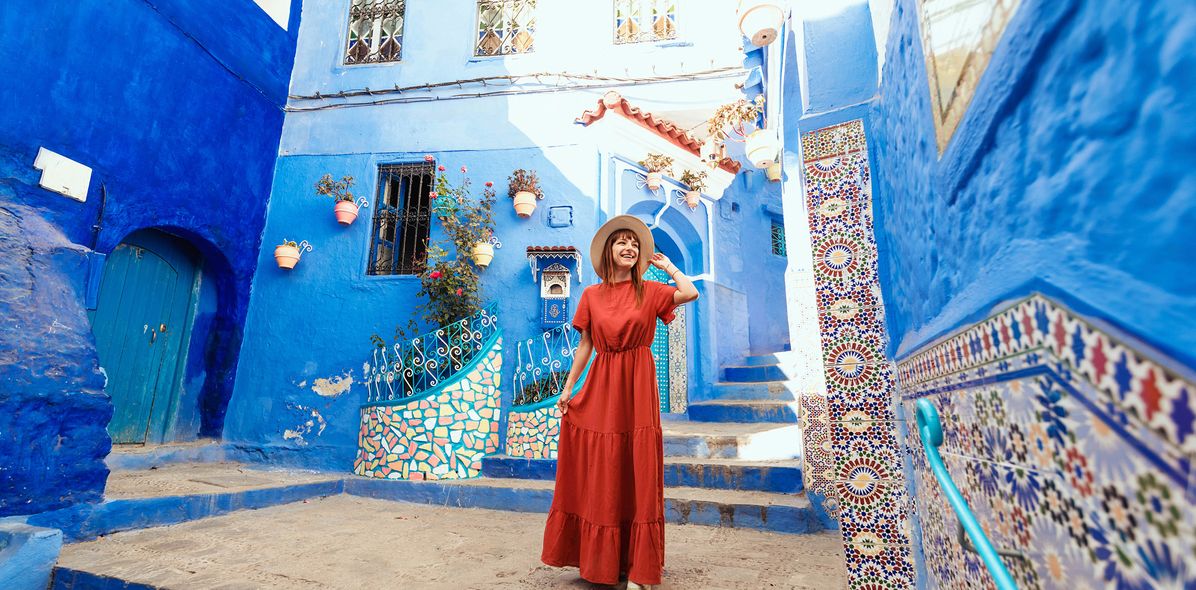 Eine Frau im roten Kleid spaziert durch die Gassen mit blauen Häusern von Chefchaouen in Marokko