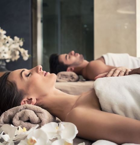 Frau und Mann liegen entspannt bei einer Partnermassage mit Blüten und Kerzen im Spa