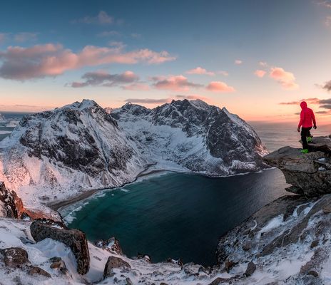 Ein Mann steht auf einem Felsen und schaut in die verschneite Fjordlandschaft Norwegens