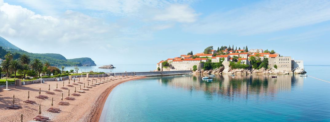 Strand mit Sonnenliegen und Blick auf Sveti Stefan in Montenegro