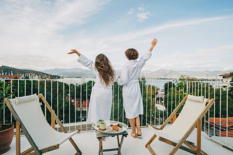 Zwei Frauen genießen den Ausblick von ihrem Hotel-Balkon auf einen Hafen