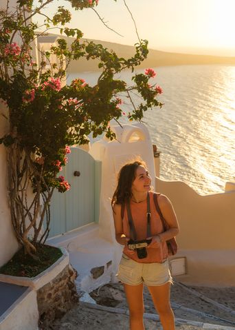 Frau mit einer Kamera in der Hand spaziert durch die Gassen von Santorin bei Sonnenuntergang