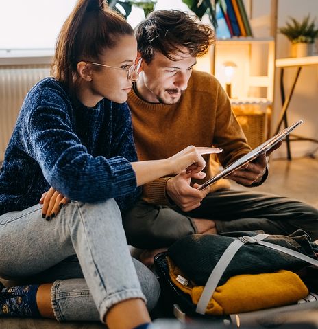 Pärchen mit Tablet beim Kofferpacken