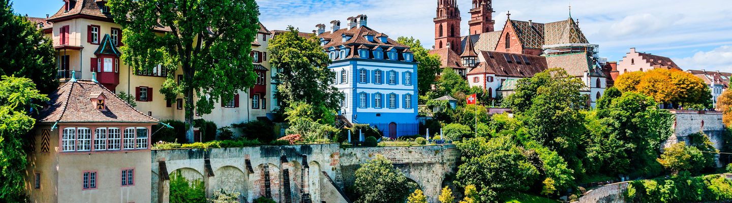 Die historische Altstadt von Basel erstreckt sich mit bunten Gebäuden und Kirchtürmen am Rheinufer.