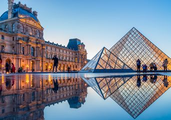 Louvre in Paris mit Glaspyramide und historischer Museumsfassade bei Sonnenuntergang