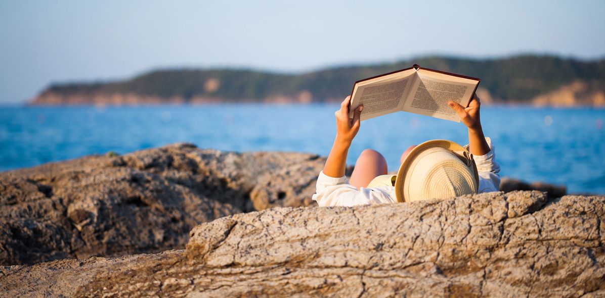 Frau auf einem Felsen buchlesend am Meer