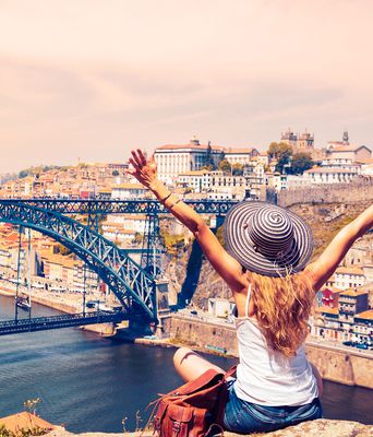 Eine Frau streckt auf einem Aussichtspunkt in Porto die Arme vor der Dom-Luís-I-Brücke aus