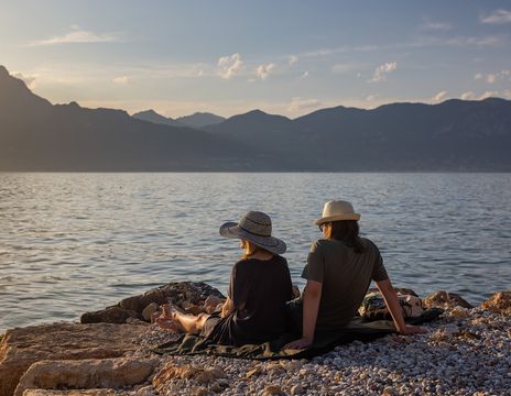 Paar sitzt am Ufer des Gardasees und genießt den Sonnenuntergang mit Blick auf die Berge