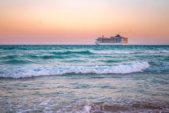 Kreuzfahrtschiff auf dem Meer bei Sonnenuntergang mit sanften Wellen und rosafarbenem Himmel
