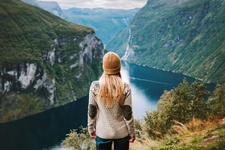 Eine Frau mit Mütze schaut auf den Geiranger Fjord hinab in Norwegen