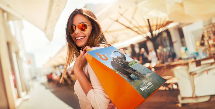 Frau mit Sonnenbrille trägt Einkaufstüte von Berge & Meer beim Bummeln im Einkaufszentrum