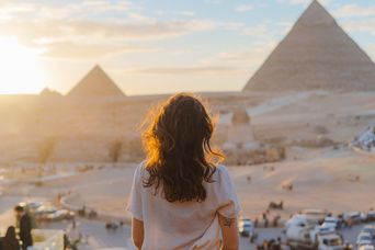 Frau in Rückansicht blickt bei Sonnenaufgang auf die Pyramiden von Gizeh in Ägypten