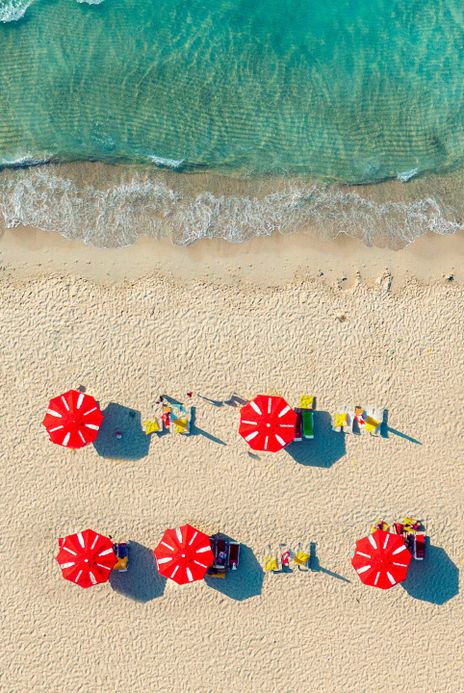 Luftaufnahme von roten Sonnenschirmen am weißen Sandstrand von Mykonos, Griechenland