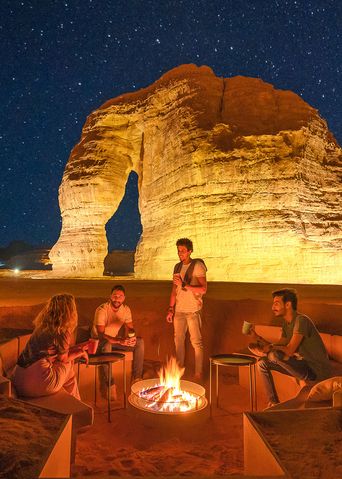 Wüstenlager bei Nacht mit Feuerstelle und beleuchteten Felsen in Saudi-Arabien