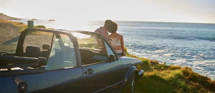 Ein Reisender sitzt auf einem Cabrio an der grünen Küste und genießt den weiten Blick auf das Meer.
