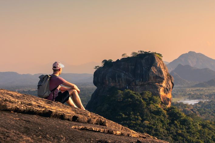Reisender sitzt auf einem Felsen mit Blick auf den berühmten Löwenfelsen Sigiriya im Zentrum Sri Lankas